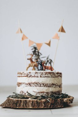 Beyaz kremalı ve bisküvili güzel pasta ahşap bir standın üzerinde duruyor ve küçük hayvanat bahçesi hayvanlarıyla süslenmiş, beyaz arka plan