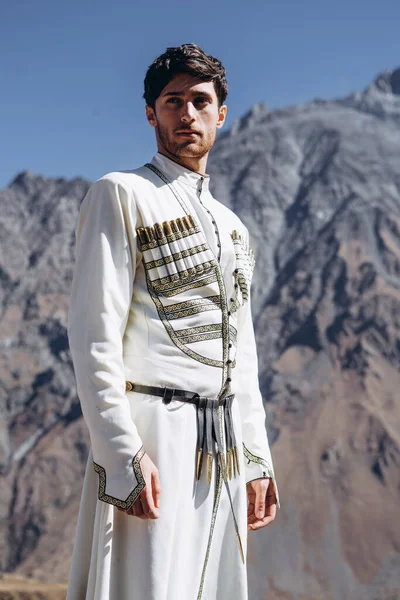 noise effect, selective focus: stylish Georgian man dressed in white national men\'s suit. Portrait of Georgian groom during wedding on Caucasus mountains