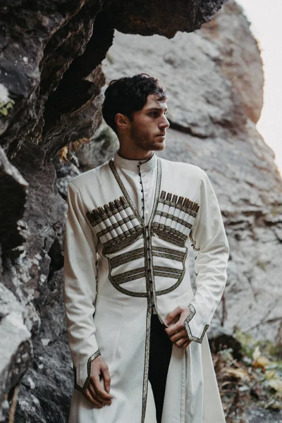 stylish Georgian man dressed in white national men\'s suit. Portrait of Georgian groom during a wedding on Caucasus mountains