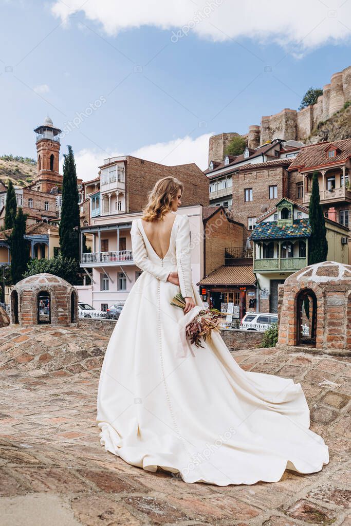 incredibly charming bride poses for a photo in a sophisticated wedding dress walking along the pretty streets of the old Georgian city of Tbilisi