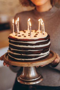 Güzel bir gülüşü olan çekici sarışın kız pasta tutuyor. Beklenmedik bir hediyeden mutlu bir doğum günü kızının duyguları: yanan mumlu ev yapımı pasta, seçici odaklanma, gürültü efekti