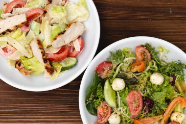 Çekici bir arkaplana yerleştirilmiş sosla karıştırılmış taze salata içerikli beyaz tabaklar. Menü, pankart veya reklam için bir yer