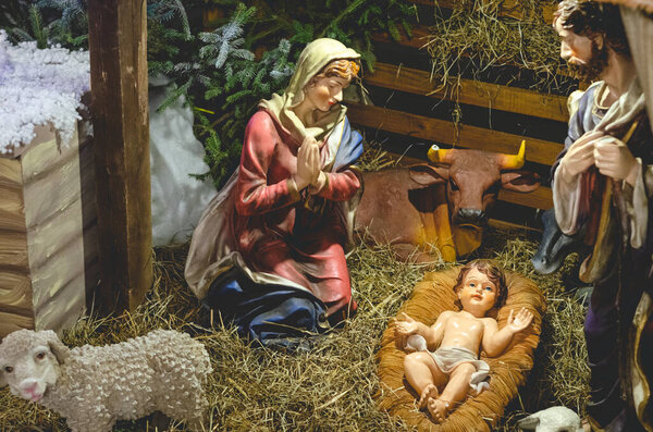 Christmas Nativity scene with The Holy Child, The Blessed Virgin Mary, Saint Joseph, ox and donkey in evening. Selective focus, noise effect