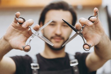 Şık ve çekici sakallı bir berber, kollarını uzattığı zaman profesyonel saç makası tutar. Makasa odaklan sen. Berber dükkanları, güzellik salonları ve kuaförler için konsept