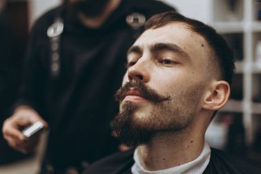 Berber dükkanında sakallı çekici bir adam. Çağdaş bir sakal şeklini retro tarzda traş eden berber, müşterisini tıraş eder.