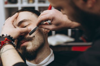 Berber dükkanında sakallı çekici bir adam. Çağdaş bir sakal şeklini retro tarzda traş eden berber, müşterisini tıraş eder.