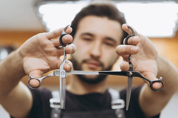 professional barber tool: sharpened scissors held by a haircut master in a modern barber shop. A concept for barbershops, beauty salons and hairdressers