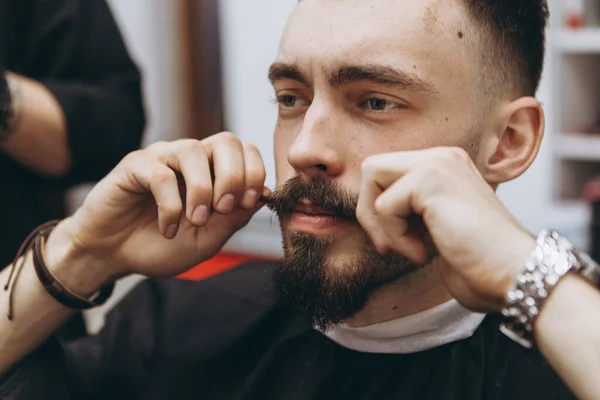 在理发店里留着胡子的英俊男子 理发师用复古的风格裁剪和模仿当代的胡子形状 给他的顾客刮胡子 — 图库照片