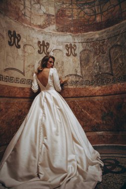 Mükemmel makyajlı zarif gelin ve güzel beyaz gelinlik romantik, karanlık bir iç mekanda fotoğraf için poz veriyor.