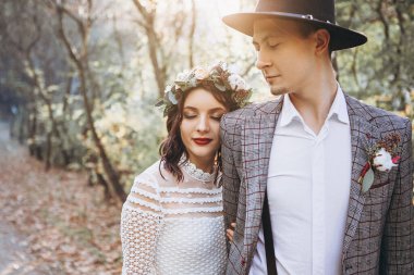 Bir çift şık gelin: smokinli ve şapkalı bir adam, kafasında çelenk olan açık beyaz elbiseli bir kadın, düğün çekimlerinde poz veren aşıklar. düğün geçmişi