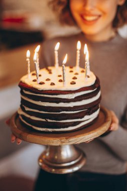 Güzel bir gülüşü olan çekici sarışın kız pasta tutuyor. Beklenmedik bir hediyeden mutlu bir doğum günü kızının duyguları: yanan mumlu ev yapımı pasta, seçici odaklanma, gürültü efekti