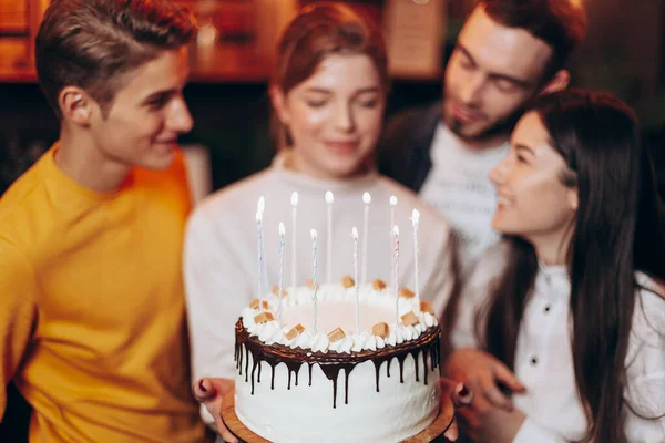 attractive girl blows out the candles on the cake and makes a wish near the best friends who came to congratulate her on her birthday