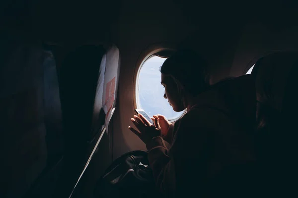girl who flies for the first time and sits on a chair by the window enjoys the view from the window, takes pictures, is happy about her first flight on the plane, selective focus, noise effect