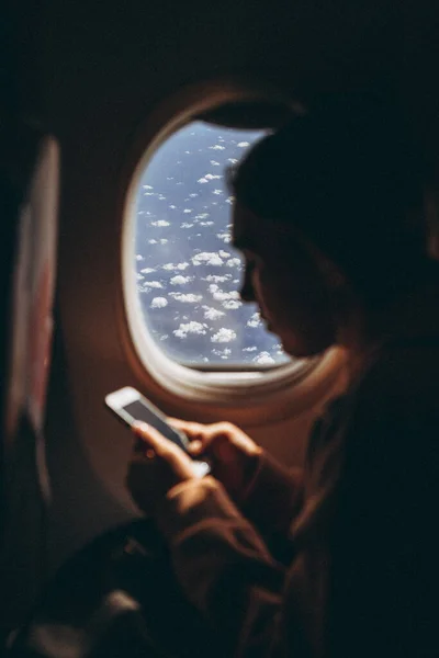 girl who flies for the first time and sits on a chair by the window enjoys the view from the window, takes pictures, is happy about her first flight on the plane, selective focus, noise effect