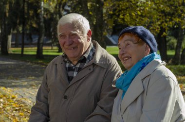 Güneşli bir günde parkta gülümseyen yaşlı, mutlu beyaz bir çift. Kıdemli çift parkta sonbahar zamanı dinleniyor. Sağlık hizmetleri yaşam tarzı yaşlılar emekliliği Sevgililer Günü konsepti
