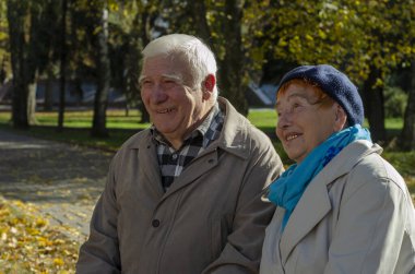 Güneşli bir günde parkta gülümseyen yaşlı, mutlu beyaz bir çift. Kıdemli çift parkta sonbahar zamanı dinleniyor. Sağlık hizmetleri yaşam tarzı yaşlılar emekliliği Sevgililer Günü konsepti