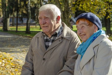 Güneşli bir günde parkta gülümseyen yaşlı, mutlu beyaz bir çift. Kıdemli çift parkta sonbahar zamanı dinleniyor. Sağlık hizmetleri yaşam tarzı yaşlılar emekliliği Sevgililer Günü konsepti