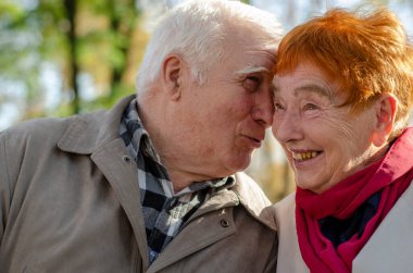 Bir kaç yaşlı insan. Gri saçlı bir adam ve parkta yan yana oturan kırmızı renkli gri saçlı bir kadın..