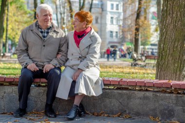 Yaşlı çift parkta dinleniyor. Dışarıda yetişkin bir çift var. Boşluğu kopyala