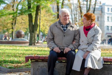 Yaşlı çift parkta dinleniyor. Dışarıda yetişkin bir çift var. Boşluğu kopyala