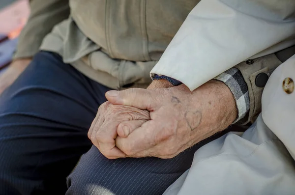 Hands in wrinkles of the old tattoo in the shape of heart. Elderly couple holding hands outdoors.