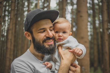 Şapkalı ve sakallı şık bir baba ormanda tatildeyken çocuğuyla oynuyor.
