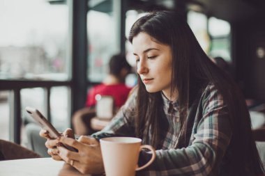 Bir cep telefonunun elinde arkadaşlarıyla sosyal ağlarda yeniden yazan ya da haber okuyan mutlu bir esmer kızın portresi.