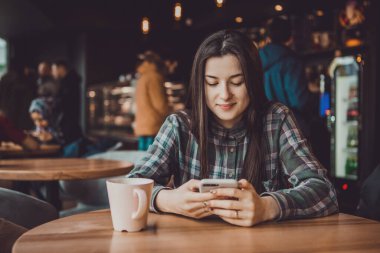 Bir cep telefonunun elinde arkadaşlarıyla sosyal ağlarda yeniden yazan ya da haber okuyan mutlu bir esmer kızın portresi.