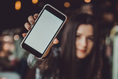 Mutluluktan gülümseyen esmer bir kızın bulanık portresi. Elinde bir cep telefonu olan ve logonuz veya ekranınız için hazır bekleyen bir kız.