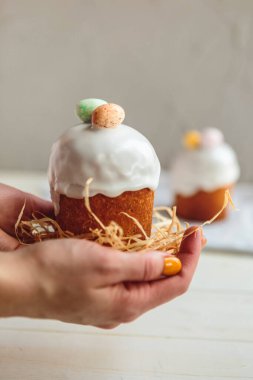 Paskalya arkaplanız kutlu olsun. Cilalı, çikolatalı ve küçük yumurtalarla süslenmiş paskalya pastası. Tebrik kartı, reklam, promosyon, poster, broşür, internet afişi, makale için resim. karmaşık kompozisyon, güzel manzara, hareket, eller