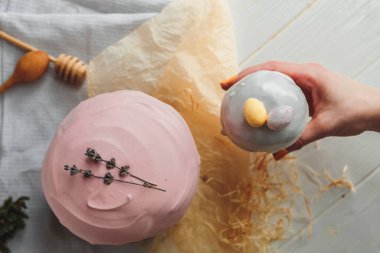 Paskalya arkaplanız kutlu olsun. Cilalı, çikolatalı ve küçük yumurtalarla süslenmiş paskalya pastası. Tebrik kartı, reklam, promosyon, poster, broşür, internet afişi, makale için resim. karmaşık kompozisyon, güzel manzara, hareket, eller