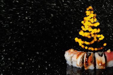 Suşi yeni yıla girer. Noel arkaplanı. Kartpostal, menü ve reklam için fikir. Işıklı bir köknar ağacının parladığı yerde, karanlık arka planda yuvarlan. Menü için dekorasyon