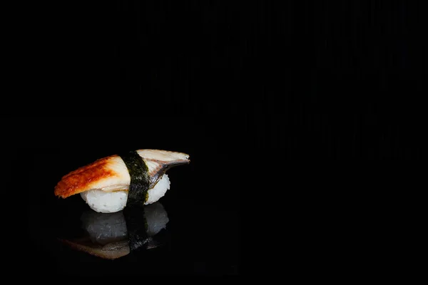 a photograph of sushi and roles on the black mirror background