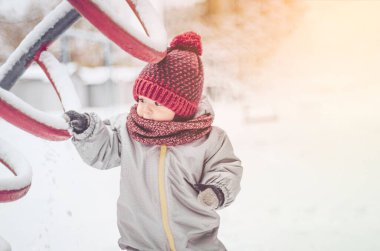 Mutlu gülümseyen çocuk güneşli kış gününde yürüyor, çocukların oyun bahçesinde karla oynuyor.