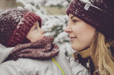 Kırmızı şapkalı, eşarplı ve kışlık eldivenli komik bir kız çocuğu güzel kış gününde kar parkında eğleniyor.