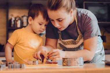 Mutfakta mutlu bir aile. Anne ve çocuk hamuru hazırlıyor, kurabiye pişiriyor. Mutfakta aile eğlencesi kavramı, çocuk çeşitli yemekler hazırlıyor: makarna, kurabiye, ekmek, zencefilli ekmek.. 