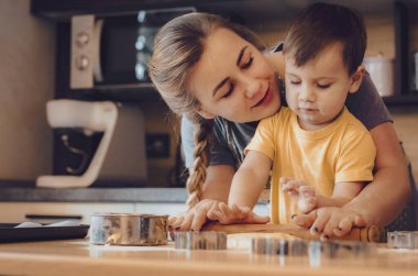 Mutlu aile birlikte fırın hazırlıyor. Anne ve çocuk çocuk kurabiye pişiriyor ve mutfakta eğleniyorlar. Ev yapımı yemek ve küçük bir yardımcı..