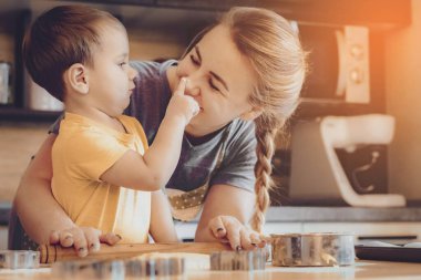 Mutlu sarışın anne ve çocuk Noel kurabiyeleri pişiriyor. Mutfakta aile eğlencesi kavramı, çocuk çeşitli yemekler hazırlıyor: makarna, kurabiye, ekmek, zencefilli ekmek..