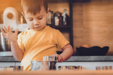 Küçük bir çocuk mutfakta hamur ve un dolu bir masanın üzerinde makarna, kurabiye, ekmek, zencefilli ekmek gibi çeşitli yemekler pişiriyor. Mutfakta aile eğlencesi kavramı, çocuk yemek hazırlıyor..