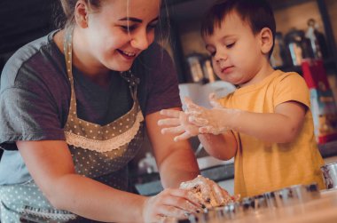 Mutfakta mutlu bir aile. Anne ve çocuk hamuru hazırlıyor, kurabiye pişiriyor. Mutfakta aile eğlencesi kavramı, çocuk çeşitli yemekler hazırlıyor: makarna, kurabiye, ekmek, zencefilli ekmek.. 