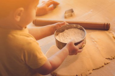 Evde mutfakta yemek pişiren sevimli çocuk. Mutfakta aile eğlencesi kavramı, çocuk çeşitli yemekler hazırlıyor: makarna, kurabiye, ekmek, zencefilli ekmek..