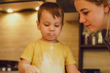 Mutlu sarışın anne ve çocuk Noel kurabiyeleri pişiriyor. Mutfakta aile eğlencesi kavramı, çocuk çeşitli yemekler hazırlıyor: makarna, kurabiye, ekmek, zencefilli ekmek..