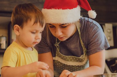 Sevimli küçük oğlan ve önlüklü güzel annesi mutfakta hamuru yoğururken gülüp oynuyorlar..