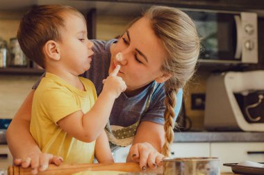 Sevimli küçük oğlan ve önlüklü güzel annesi mutfakta hamuru yoğururken gülüp oynuyorlar..