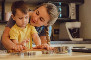 Mutlu aile birlikte fırın hazırlıyor. Anne ve çocuk çocuk kurabiye pişiriyor ve mutfakta eğleniyorlar. Ev yapımı yemek ve küçük bir yardımcı..