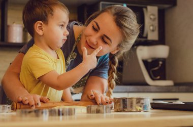 Mutlu aile birlikte fırın hazırlıyor. Anne ve çocuk çocuk kurabiye pişiriyor ve mutfakta eğleniyorlar. Ev yapımı yemek ve küçük bir yardımcı..