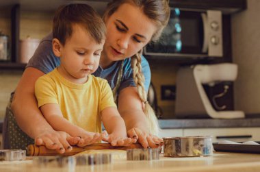 Mutfakta mutlu bir aile. Anne ve çocuk hamuru hazırlıyor, kurabiye pişiriyor. Mutfakta aile eğlencesi kavramı, çocuk çeşitli yemekler hazırlıyor: makarna, kurabiye, ekmek, zencefilli ekmek.. 