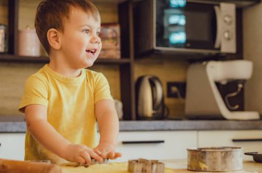 Evde mutfakta yemek pişiren sevimli çocuk. Mutfakta aile eğlencesi kavramı, çocuk çeşitli yemekler hazırlıyor: makarna, kurabiye, ekmek, zencefilli ekmek..