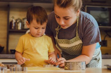 Mutfakta mutlu bir aile. Anne ve çocuk hamuru hazırlıyor, kurabiye pişiriyor. Mutfakta aile eğlencesi kavramı, çocuk çeşitli yemekler hazırlıyor: makarna, kurabiye, ekmek, zencefilli ekmek.. 