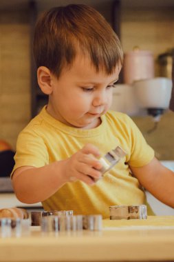 Küçük tatlı çocuk, ev mutfağında pasta yapmayı öğreniyor. Mutfakta aile eğlencesi, çocuk yemek hazırlama, çeşitli yemekler: makarna, kurabiye, ekmek, zencefilli ekmek. Klasik renk tonu. 